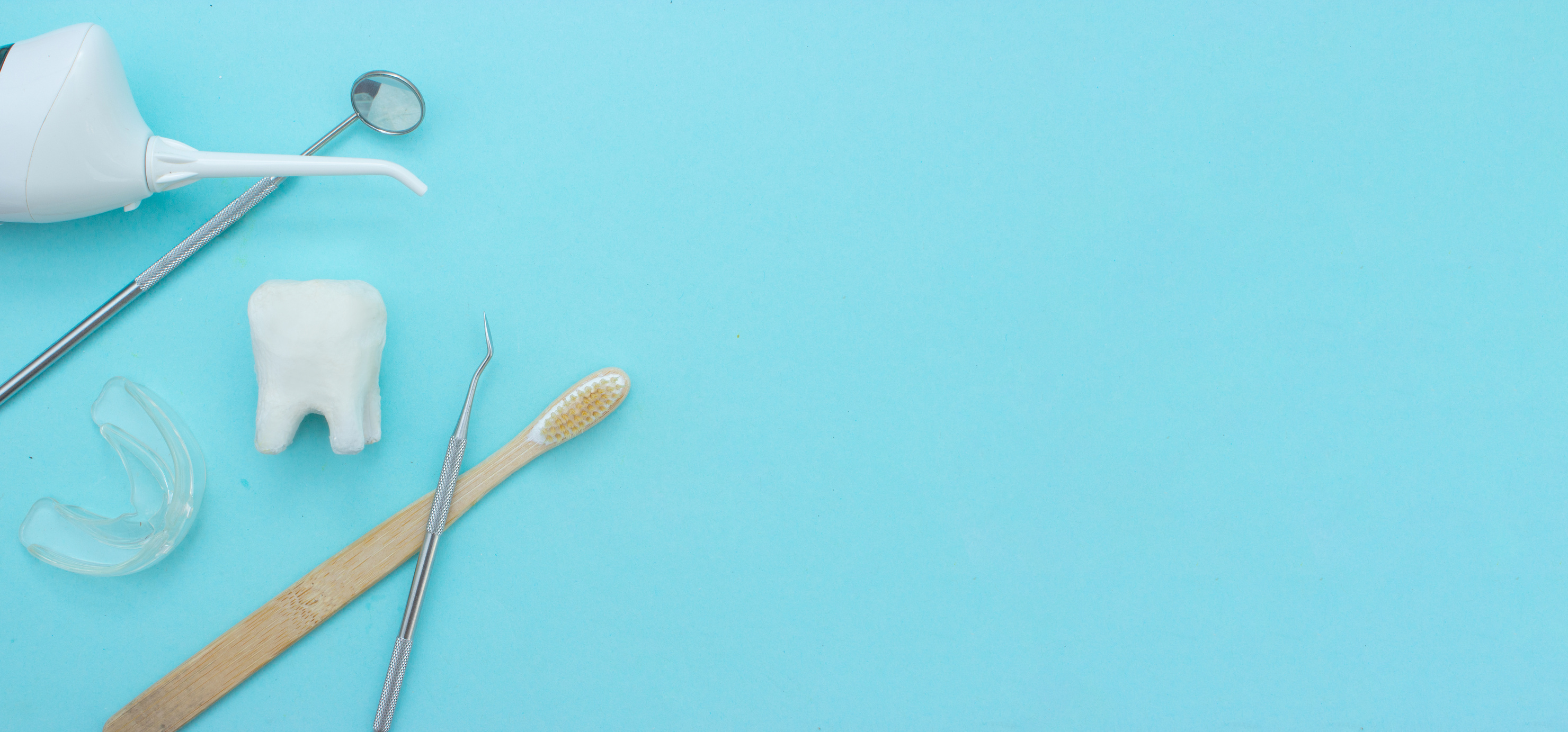 Different tools for dental care, toothbrush, dentist mirror, irrigator, removable braces, tooth mold and white tooth molar model on Blue background. Dental background. With copy space, close-up. Oral dental hygiene concept.